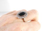 a woman ' s hand holding a ring with a black stone