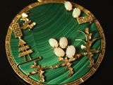 a green and gold pendant with flowers on it