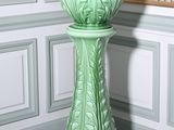 un vase vert posé par terre devant un mur