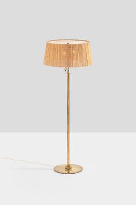 a gold floor lamp with a beige shade on top of it
