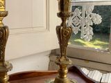 two gold candles on a wooden table in front of a window