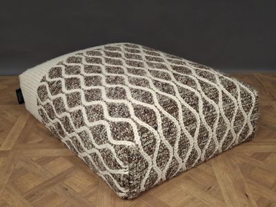 un pouflet marron et blanc posé sur un parquet, avec un mur gris en arrière-plan