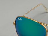 Lunettes de soleil Ray-Ban avec verres verts miroités, posées sur une surface blanche