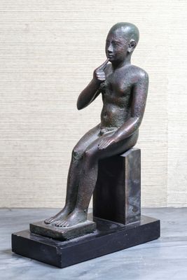 statue d'un garçon assis sur un bloc, la main posée sur le menton