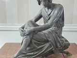 statue of a woman sitting on a wooden table with her hands on her knees