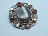 a close up of a silver broochle with garnets on it