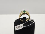 une bague en or sertie d'une pierre verte repose sur un présentoir à bagues noir