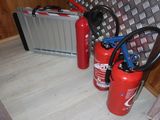 two fire extinguisors next to a suitcase on the floor