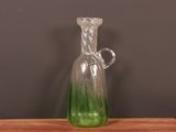 un vase en verre vert muni d'une anse, posé sur une table en bois