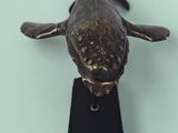bronze sculpture of a fish on a black stand on a green surface