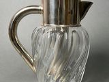a glass pitcher with a metal handle on a table