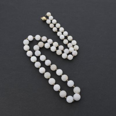 un collier de perles blanches muni d'un fermoir doré, sur fond noir