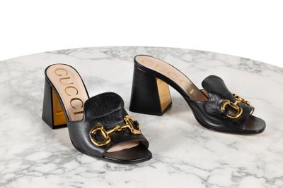 une paire de mules en cuir noir ornées d'une boucle dorée au talon