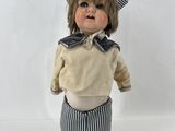 une petite poupée qui porte un chapeau et un pantalon