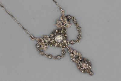 une photo d'un collier composé d'une croix en argent ornée d'un motif floral, suspendue à une chaîne