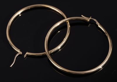 une paire de boucles d'oreilles créoles en or posées sur une surface noire