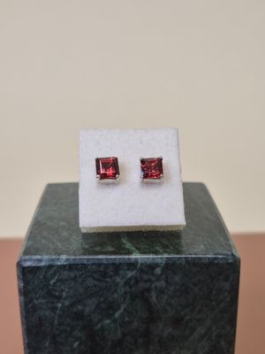 a pair of red stone stud earrings sitting on top of a marble block