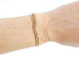 someone is wearing a gold bracelet with a greek design on it