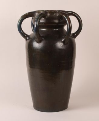 un vase noir muni de deux anses, posé sur une surface blanche
