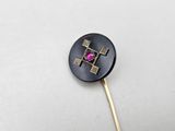 a close up of a black and gold pin with a pink stone