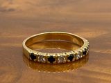bague en or jaune sertie de diamants noirs et blancs sur un support en bois