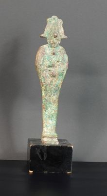 une statue égyptienne représentant une femme tenant un oiseau, posée sur un socle noir