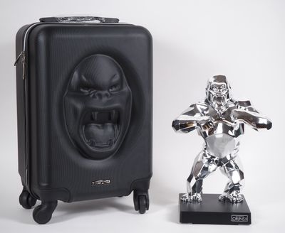 une statue en argent représentant un gorille, à côté d'une valise noire