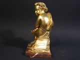 gold statue of a man sitting on a marble block with his hands on his knees