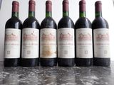 six bottles of red wine are lined up on a table