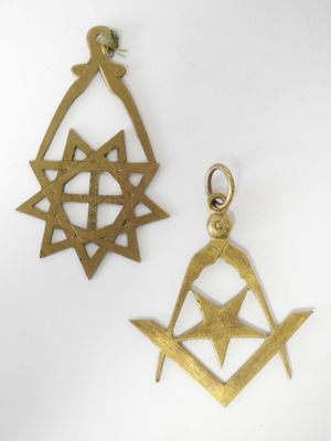 deux pendentifs en laiton ornés de symboles maçonniques, posés sur une surface blanche