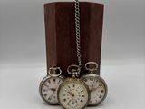 trois montres de poche en argent posées sur un socle en bois