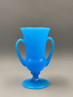 a blue glass vase with a handle on a table
