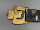 gold and black leather belt with a metal buckle on a gray surface
