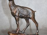 statue en bronze représentant une chèvre posée sur un rocher, sur fond gris