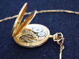 a gold pocket watch on a chain on a blue surface