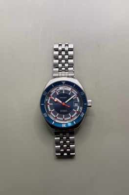 un gros plan d'une montre montée sur un bracelet en métal, posée sur une surface blanche