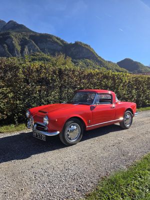 une vieille voiture rouge garée au bord d'un chemin de terre