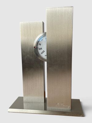 une horloge en métal posée sur un socle, sur fond blanc
