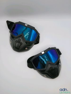 une paire de lunettes de protection noires aux verres miroités bleus posée sur une surface blanche