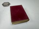 a small red book sitting on a table next to a small metal object