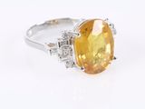 a close up of a yellow sapphire and diamond ring on a white surface