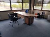 a desk and chairs in an empty room with large windows
