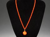 an orange beaded necklace with a pendant on a black mannequin