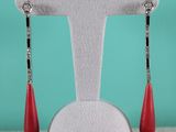 une paire de boucles d'oreilles rouges en forme de goutte, posées sur un socle blanc devant un fond turquoise