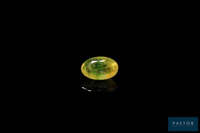 a close up of a yellow and green gemstone on a black surface