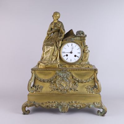 a gold clock with a woman sitting on top of it