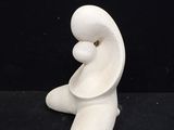 a white sculpture of a person sitting on a black surface