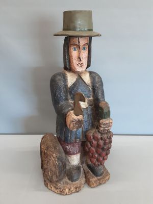figurine en bois représentant un homme coiffé d'un chapeau et tenant une grappe de raisin