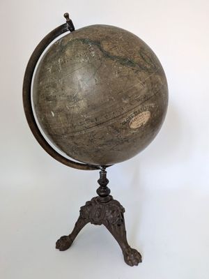un vieux globe terrestre posé sur un trépied, adossé à un mur blanc