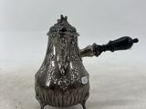 une théière ancienne en argent avec une poignée noire sur une surface blanche